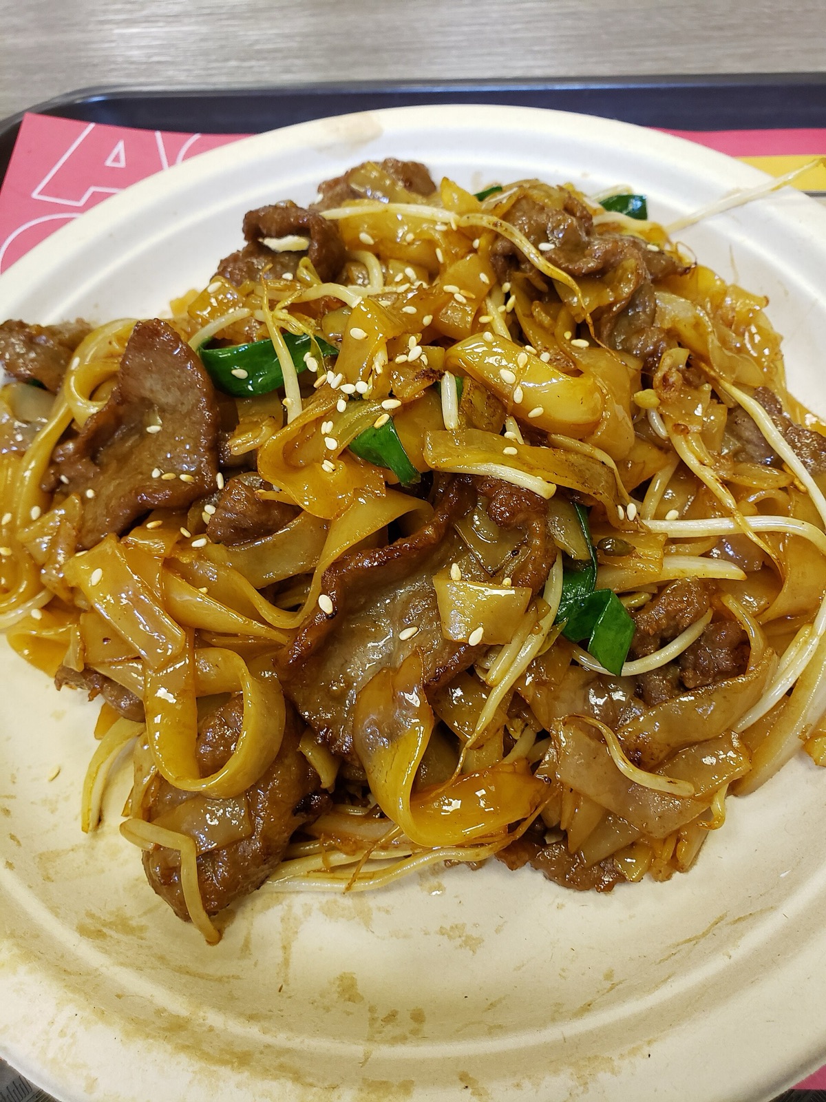 Beef chow fun heaped on a plate, scattered with toasted sesame seeds and green chilli